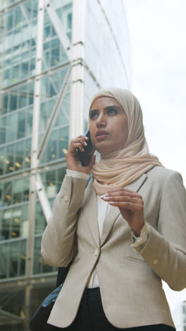 Vertikales-Video-Einer-Muslimischen-Geschäftsfrau-Mit-Mobiltelefon,-Die-Vor-Dem-Büro-In-Stadt-2-Steht